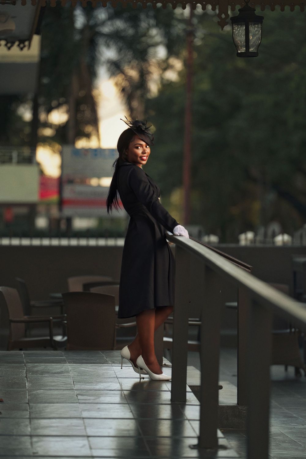 A stylish silhouette in a black outfit poses dramatically against an urban backdrop at sunset.