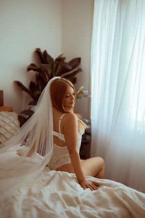 Romantic boudoir photo series showing a bride in white lingerie and veil posing elegantly on a bed.