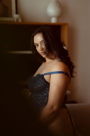 A boudoir photoshoot features dramatic lighting and black lace lingerie in an intimate indoor setting.