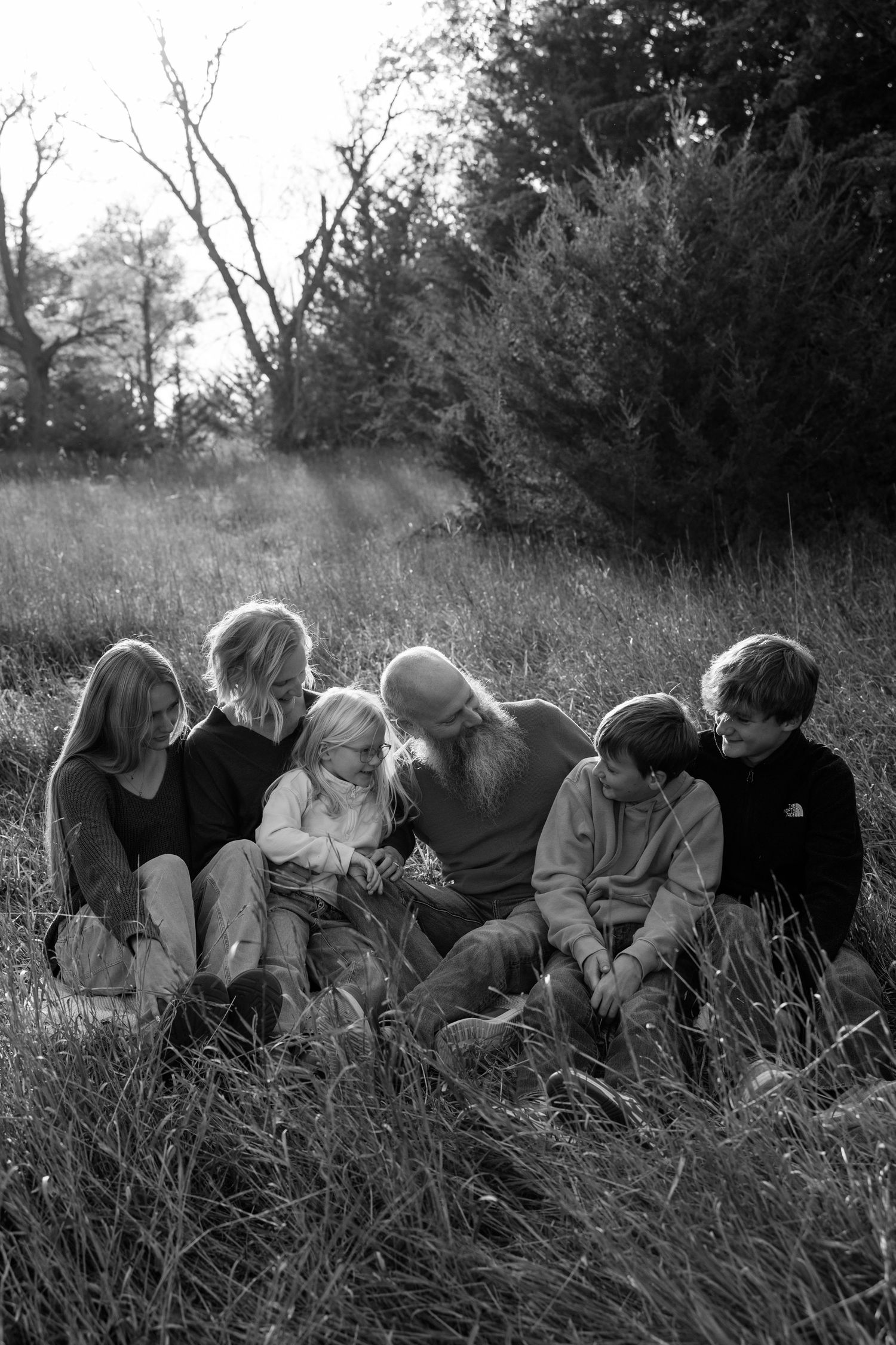 A black and white photograph of a group sitting together in a grassy field on a sunny day.