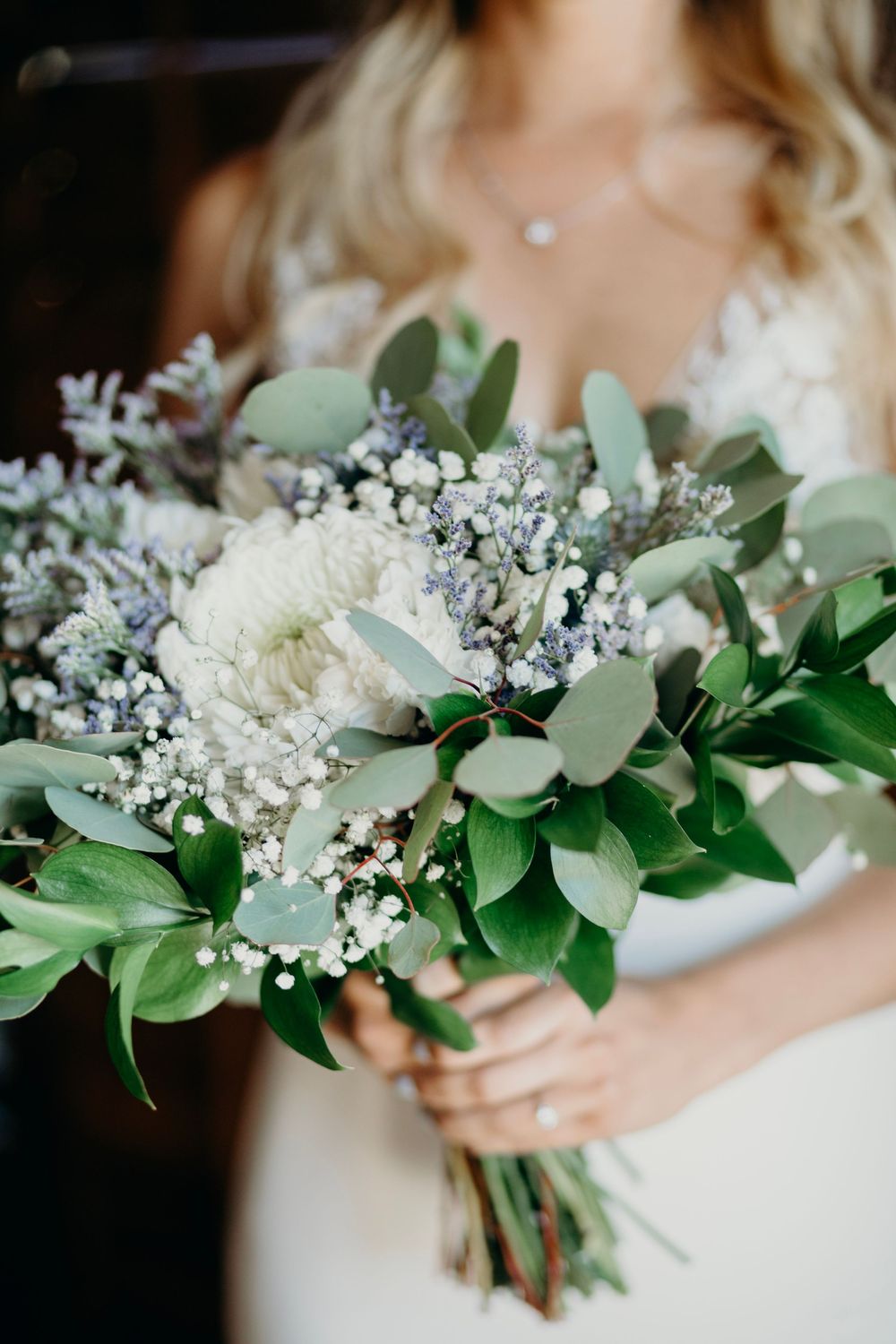 Wedding bouquet with white flowers, baby's breath, and fresh green eucalyptus leaves creates an elegant natural arrangement.