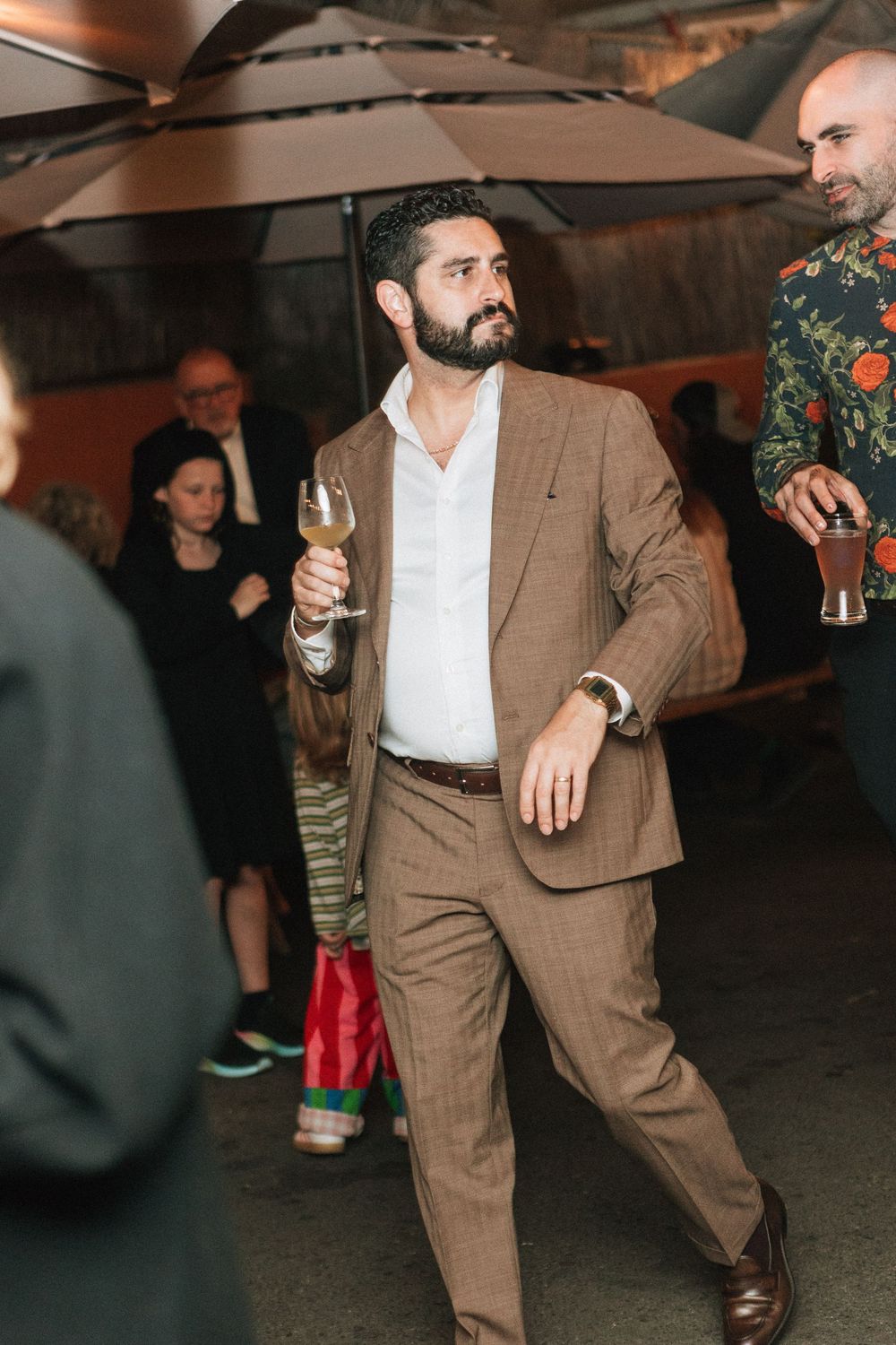 Captured on digital photography a guest in a brown suit carries a beer at wedding reeption.