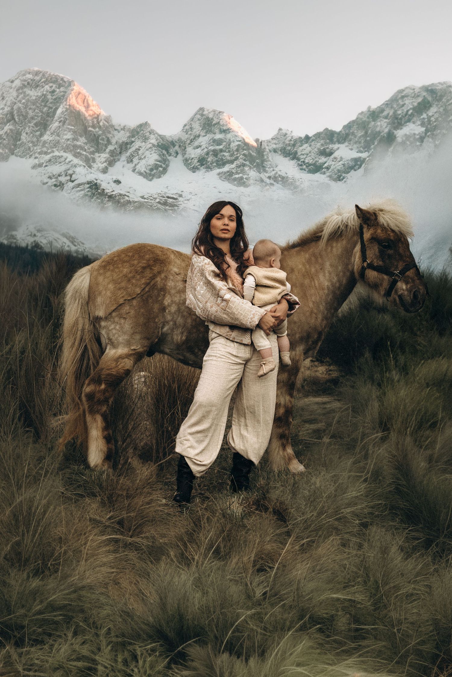 A woman in a beige outfit embraces a large brown horse in a mountainous landscape at sunset. Javea photographer