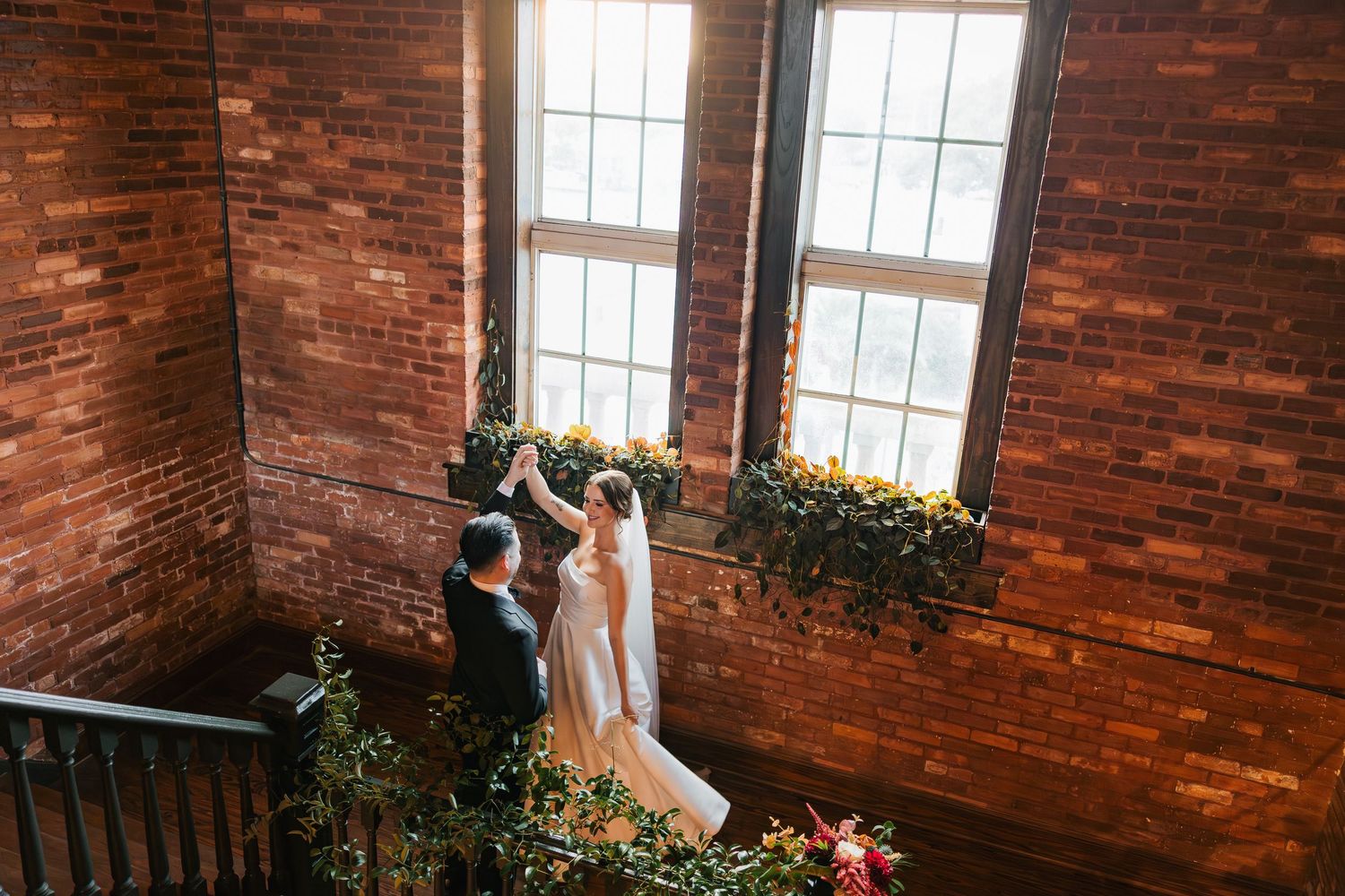 A bride and groom share a joyful moment on a staircase surrounded by lush greenery and brick walls.