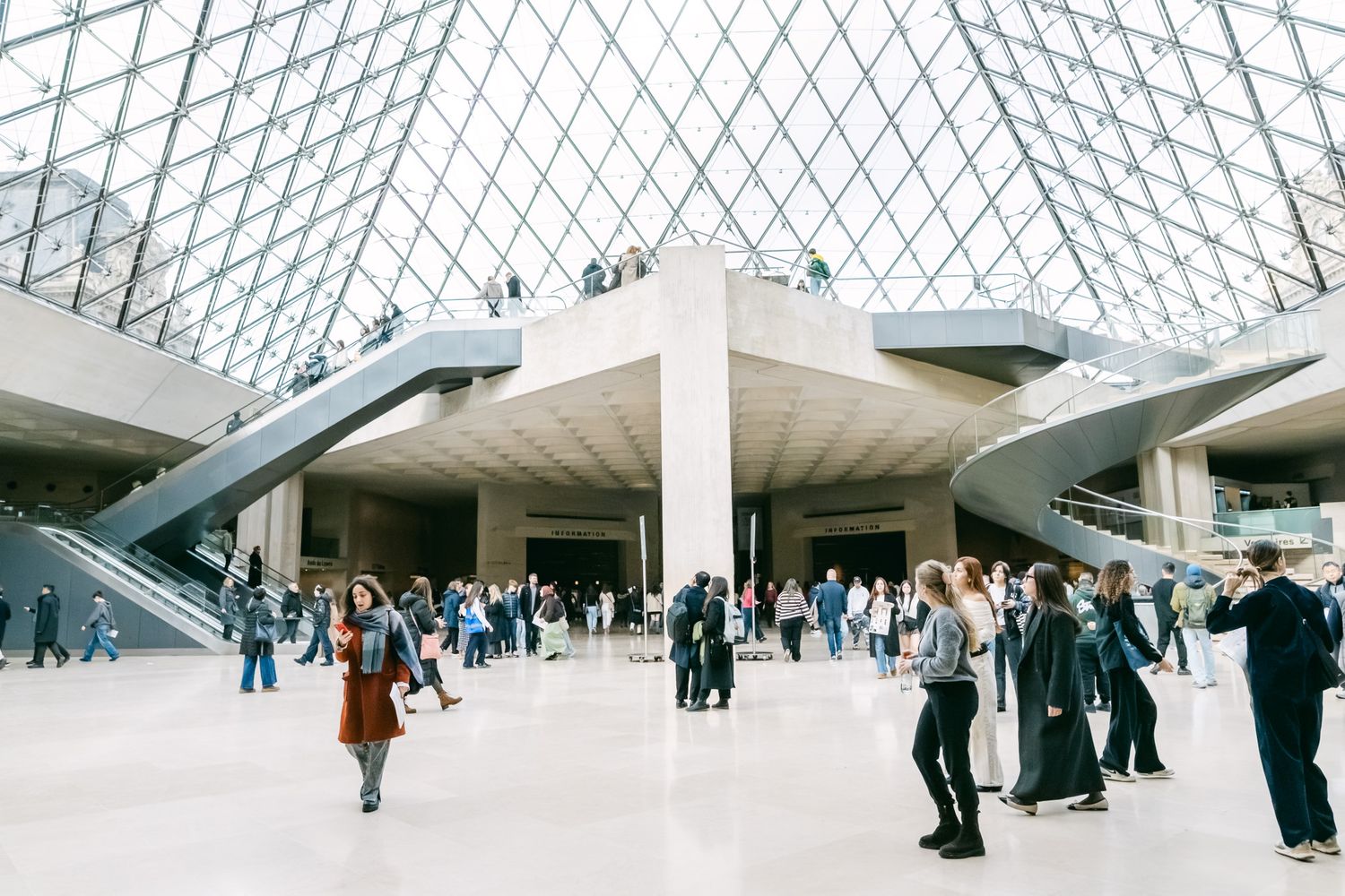 Wide panoramic view of a modern museum interior with geometric glass ceiling and visitors exploring the exhibits.