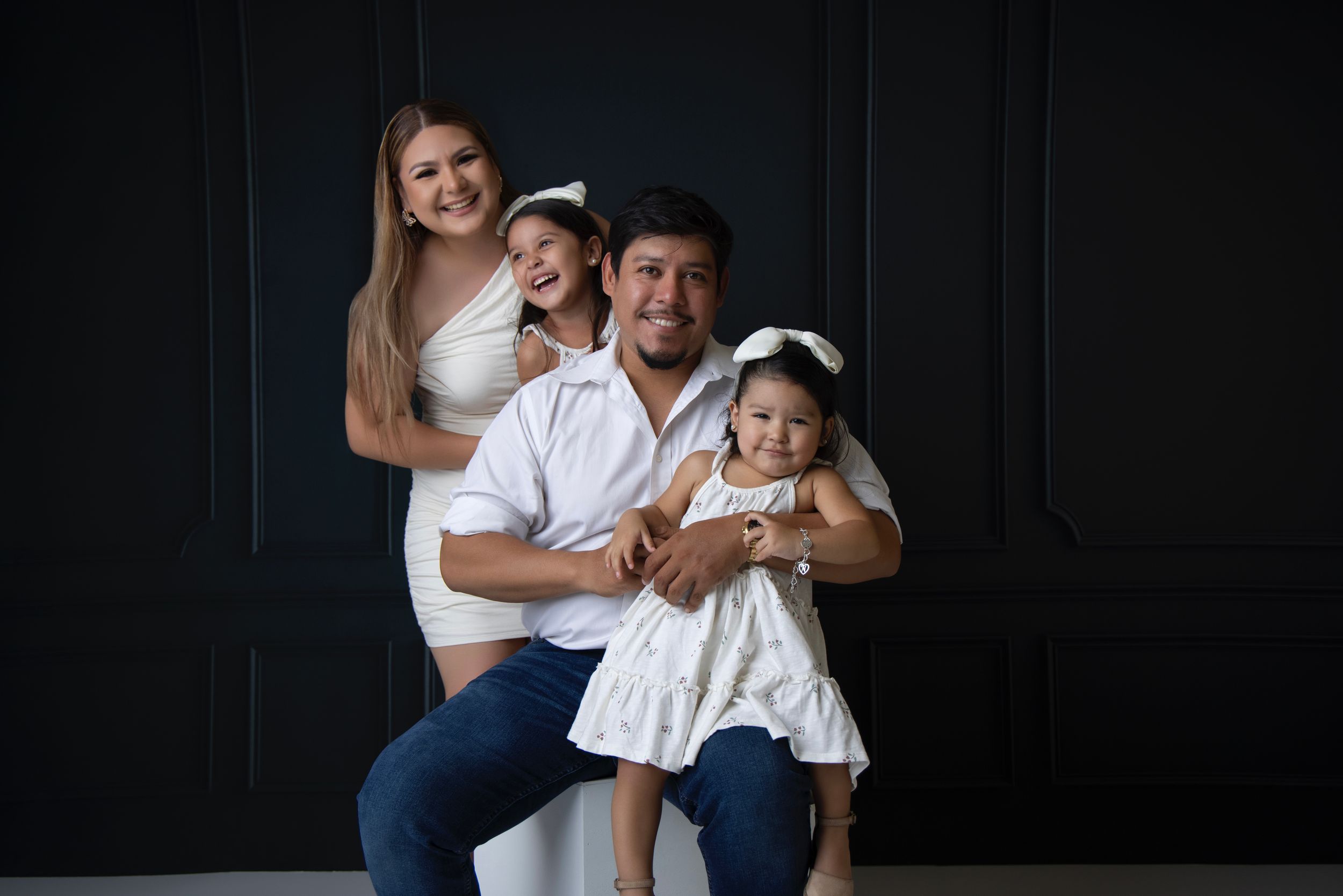 Sweet family interactions photographed against dark backdrop in coordinated outfits.