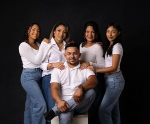 Family wearing white shirts and jeans poses against black background.