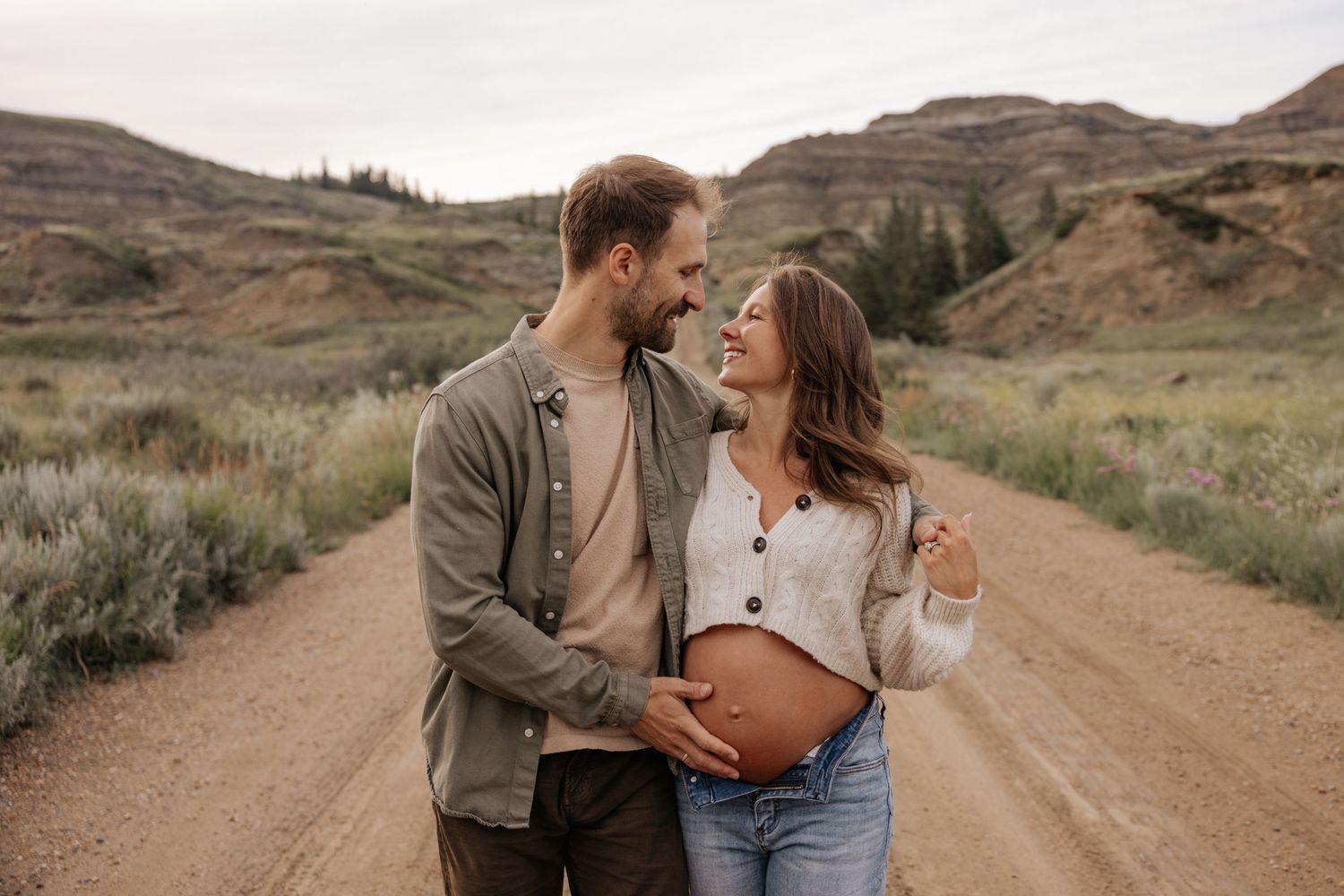 Pregnant woman in denim and boots poses in front of rugged badlands landscape during golden hour.