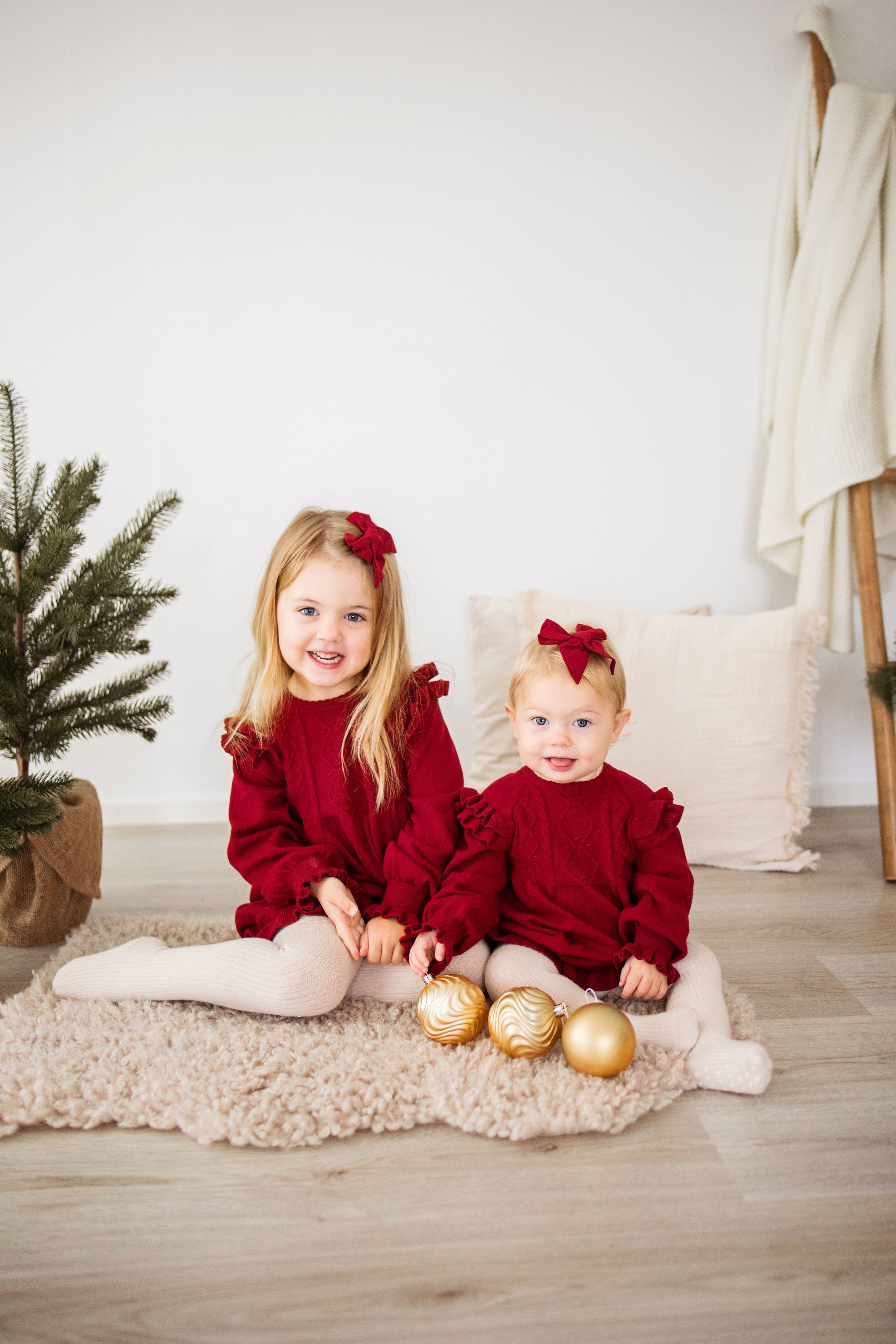 Three festive holiday photos featuring matching burgundy outfits and gold ornaments on a light carpet beside decorative greenery.