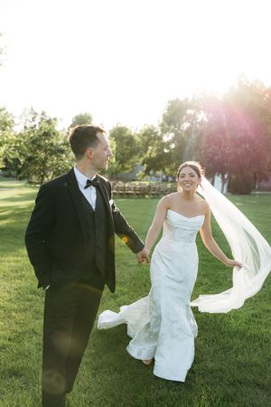 Sunlit wedding couple playfully interacts in a grassy field during sunset creating joyful candid moments.