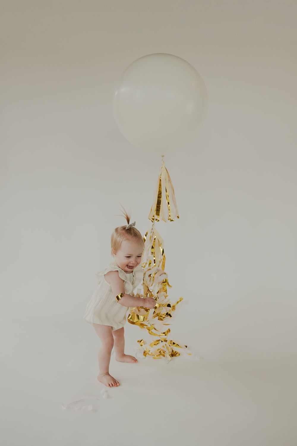 Five sequential photos show a baby in white clothing playing with falling gold confetti against a light background.