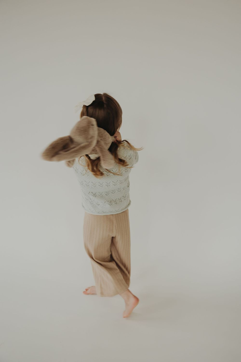 Person wearing a white lace top and beige pants dances gracefully against neutral background.
