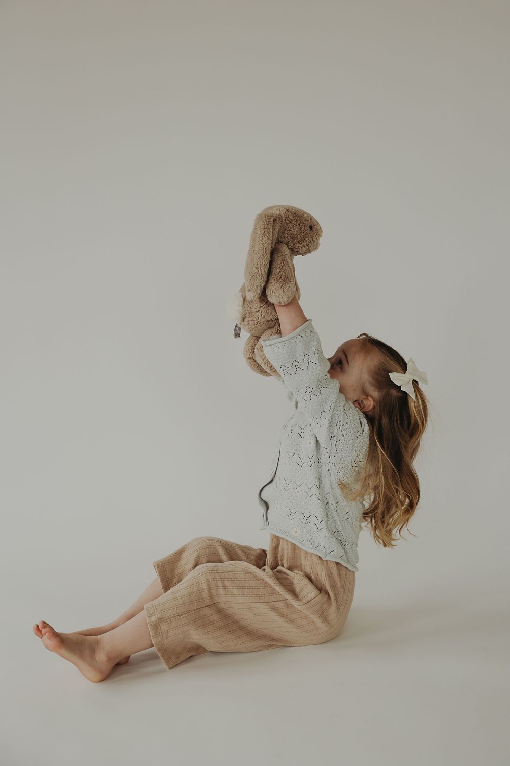 A figure reclining in soft knit clothing on a light colored floor in an artistic minimalist pose.