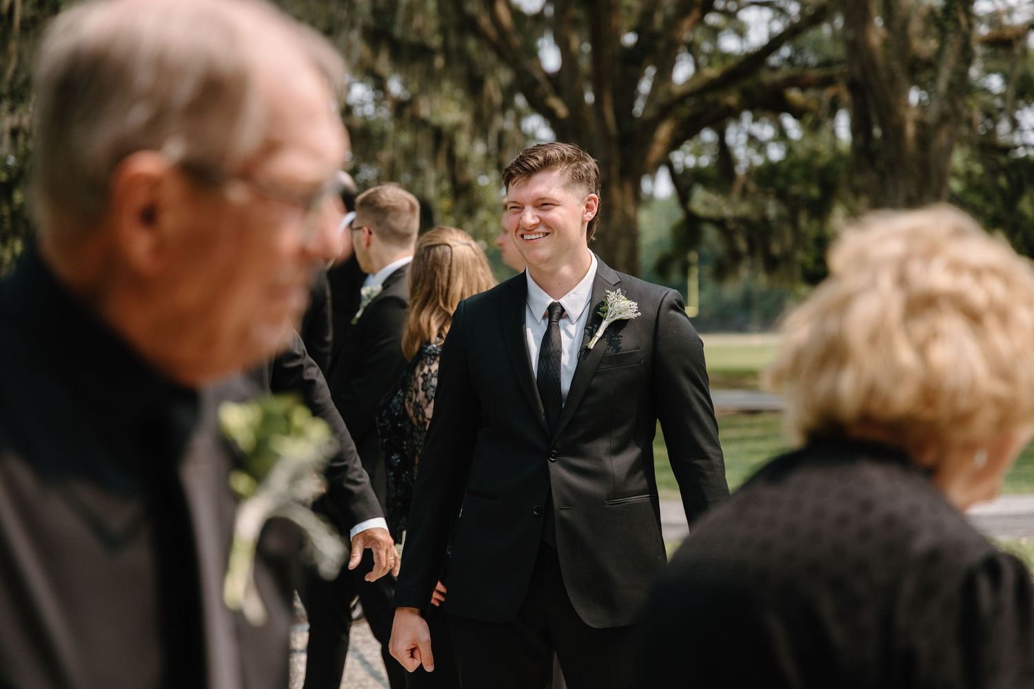 A joyous moment at an outdoor wedding ceremony with guests gathered under Spanish moss draped trees.