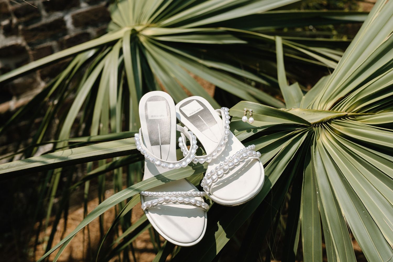 White wedding shoes are elegantly displayed among tropical palm fronds and greenery in an outdoor garden setting.