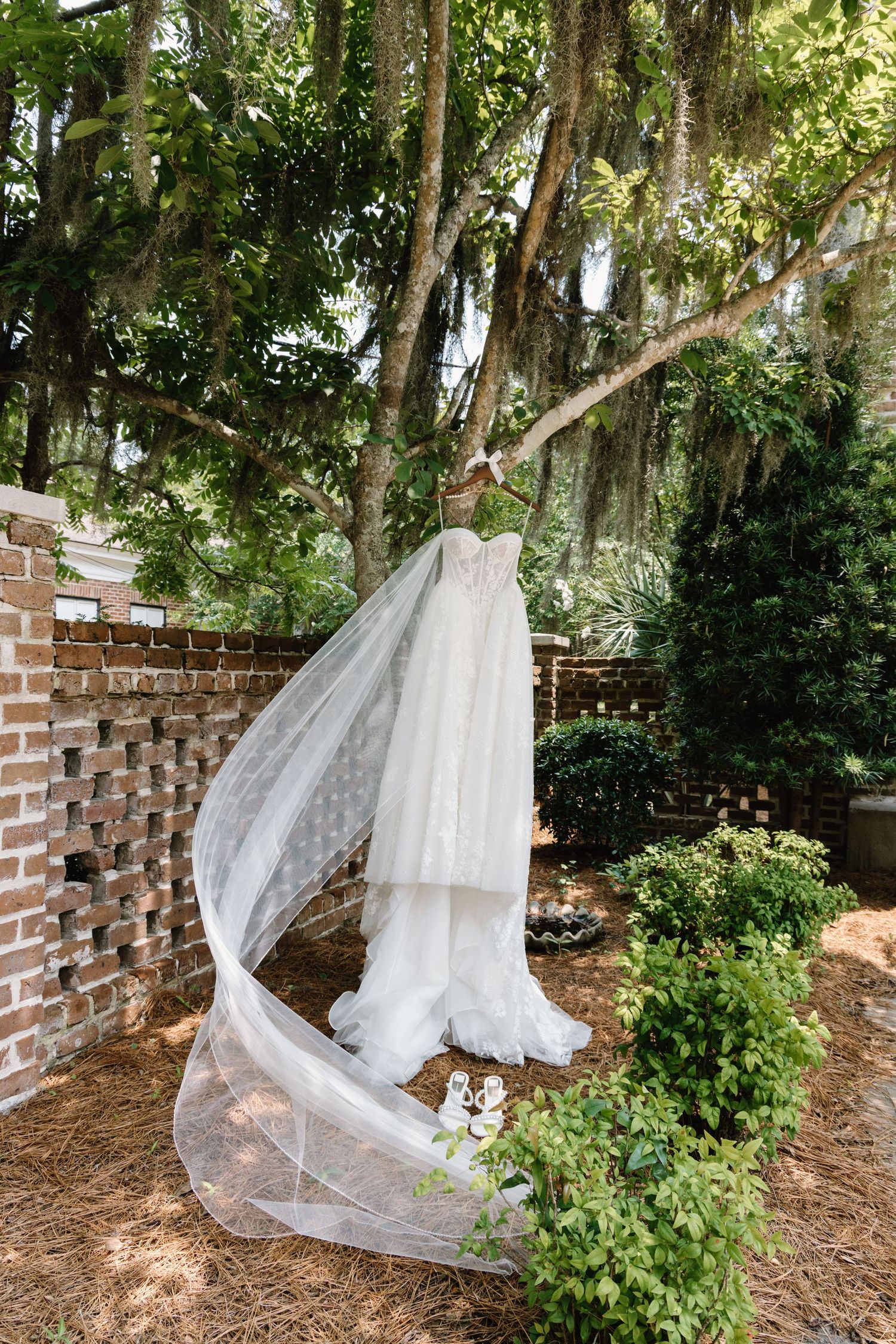 A long white wedding veil draped on a garden wall with brick columns and lush greenery in the background.