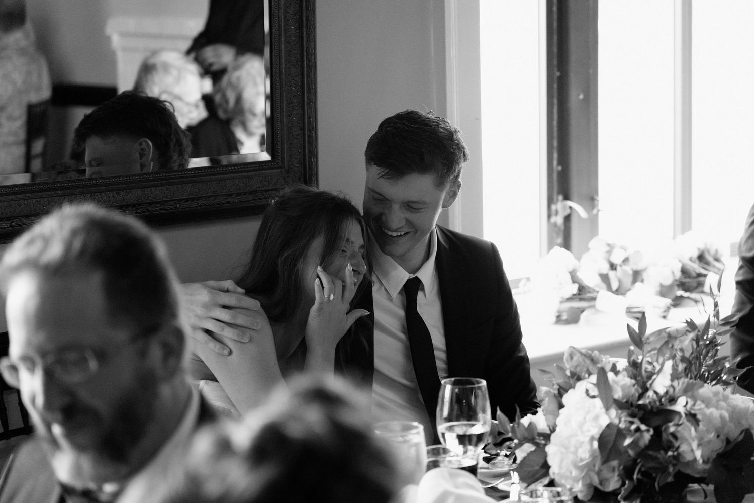 Black and white photograph of restaurant patrons dining in an elegant setting surrounded by floral arrangements.