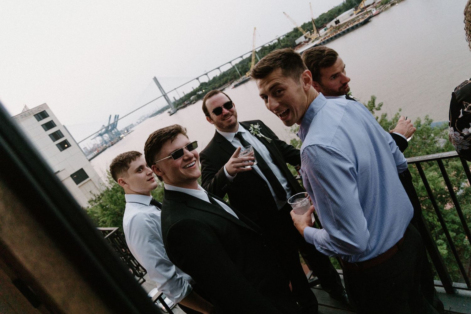 A group wearing formal attire shares a lighthearted moment together on an outdoor balcony or terrace.
