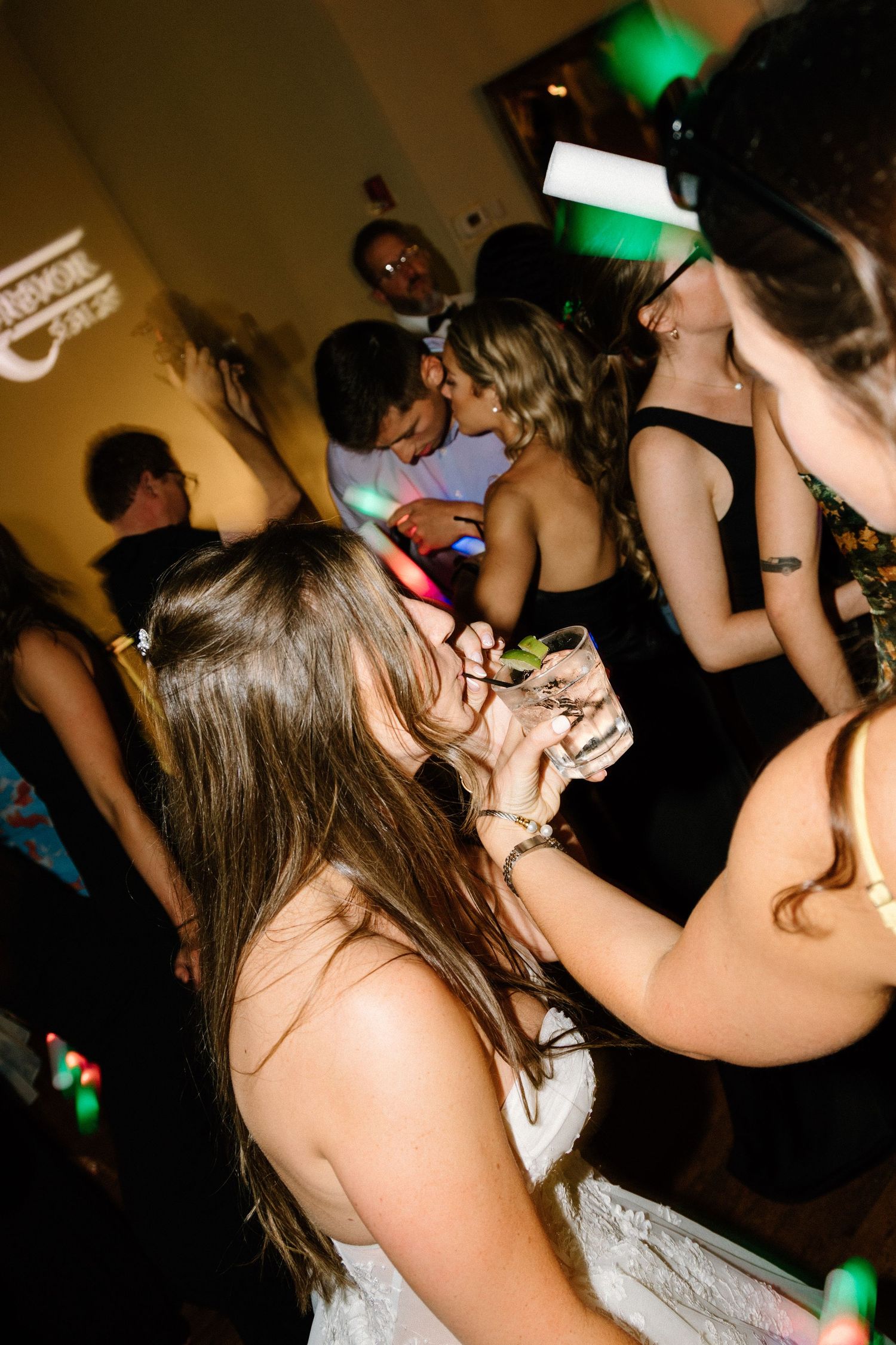 People dancing and enjoying themselves at a dark nightclub with green lighting effects and strobe lights visible.