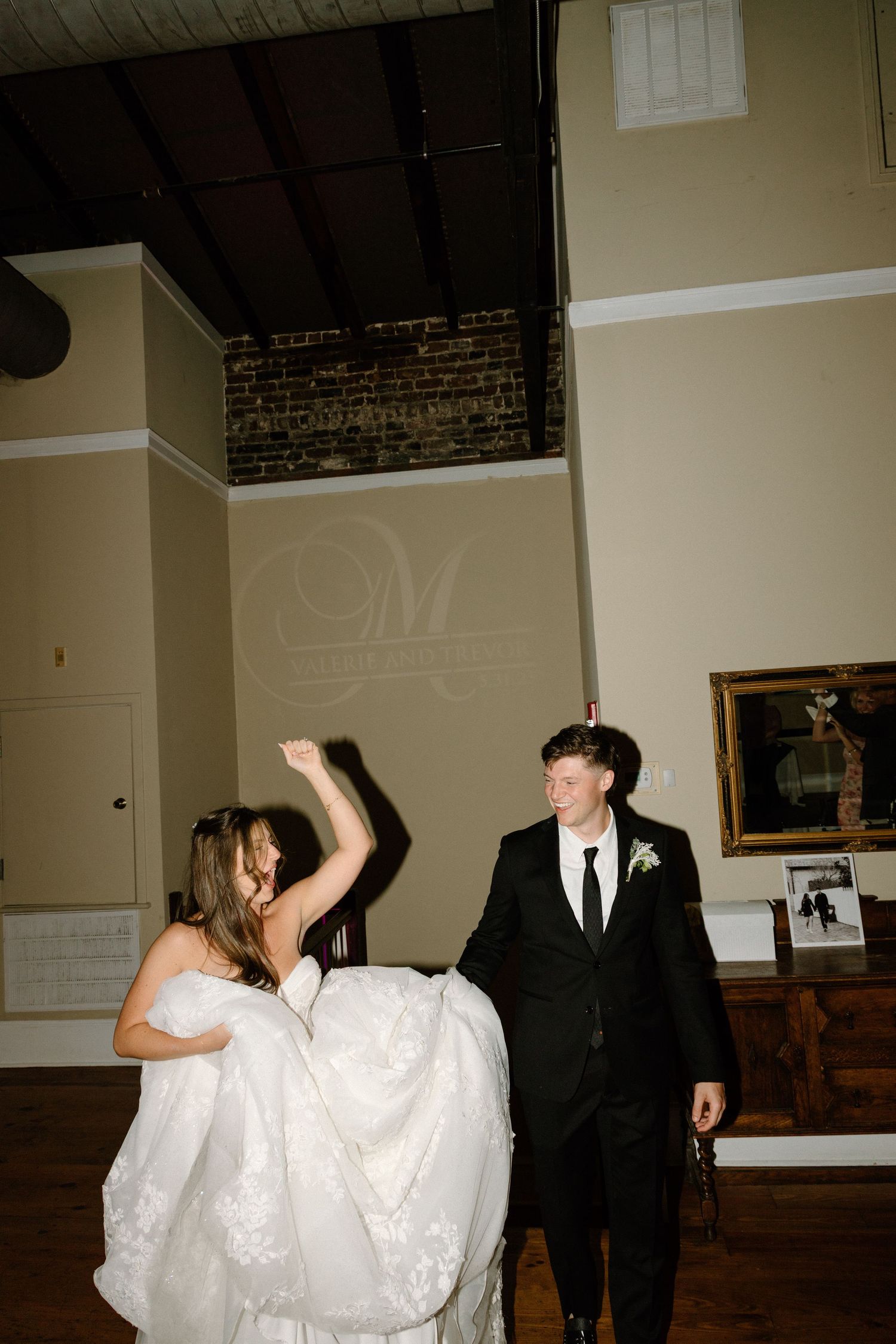A happy couple dances at their wedding reception with the bride wearing a white gown with flowing lace details.