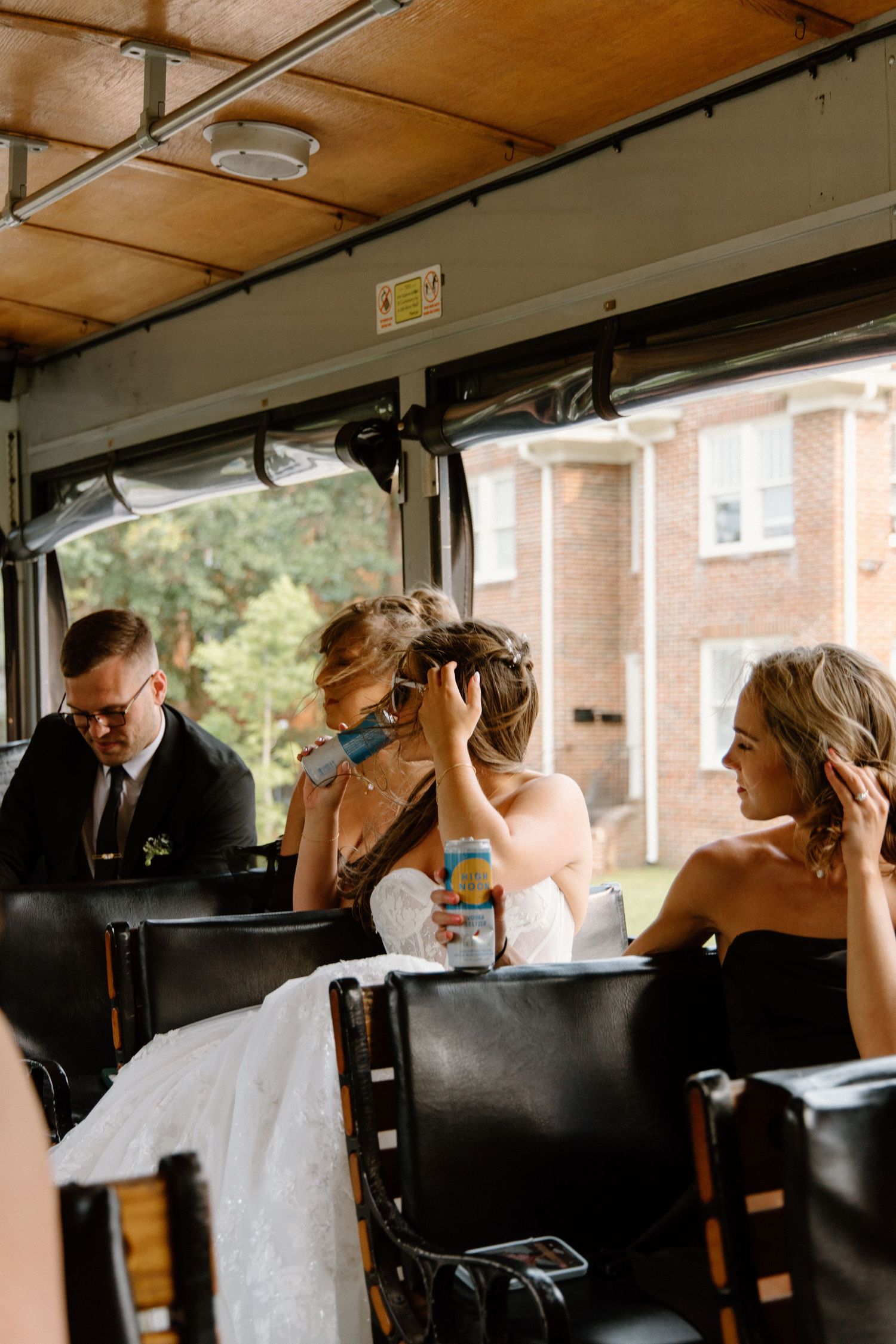 Inside a vintage bus or trolley, a couple in wedding attire shares a moment while a driver navigates at the front.