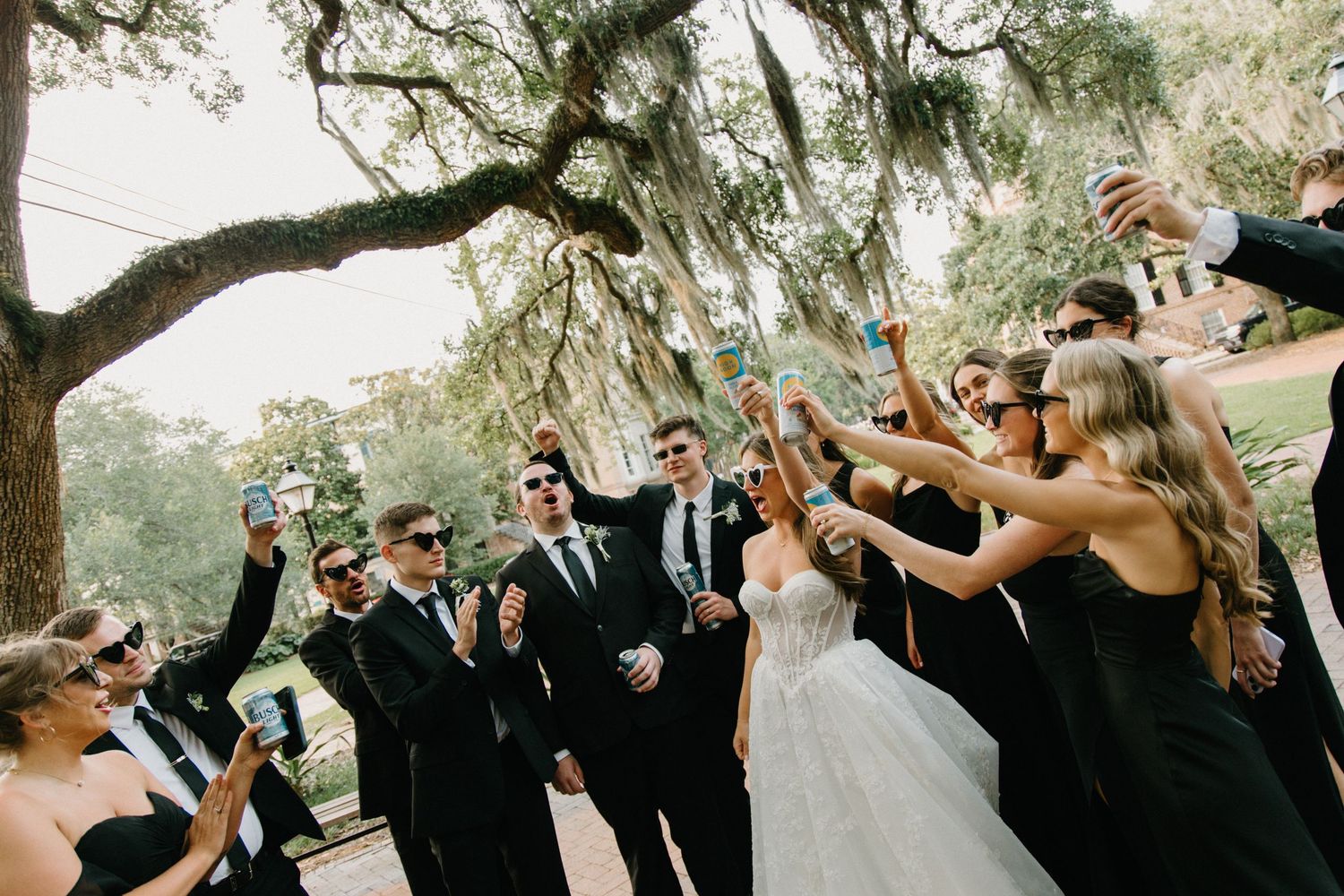 Wedding guests jump with joy in a celebratory group photo under trees at an outdoor reception celebration.