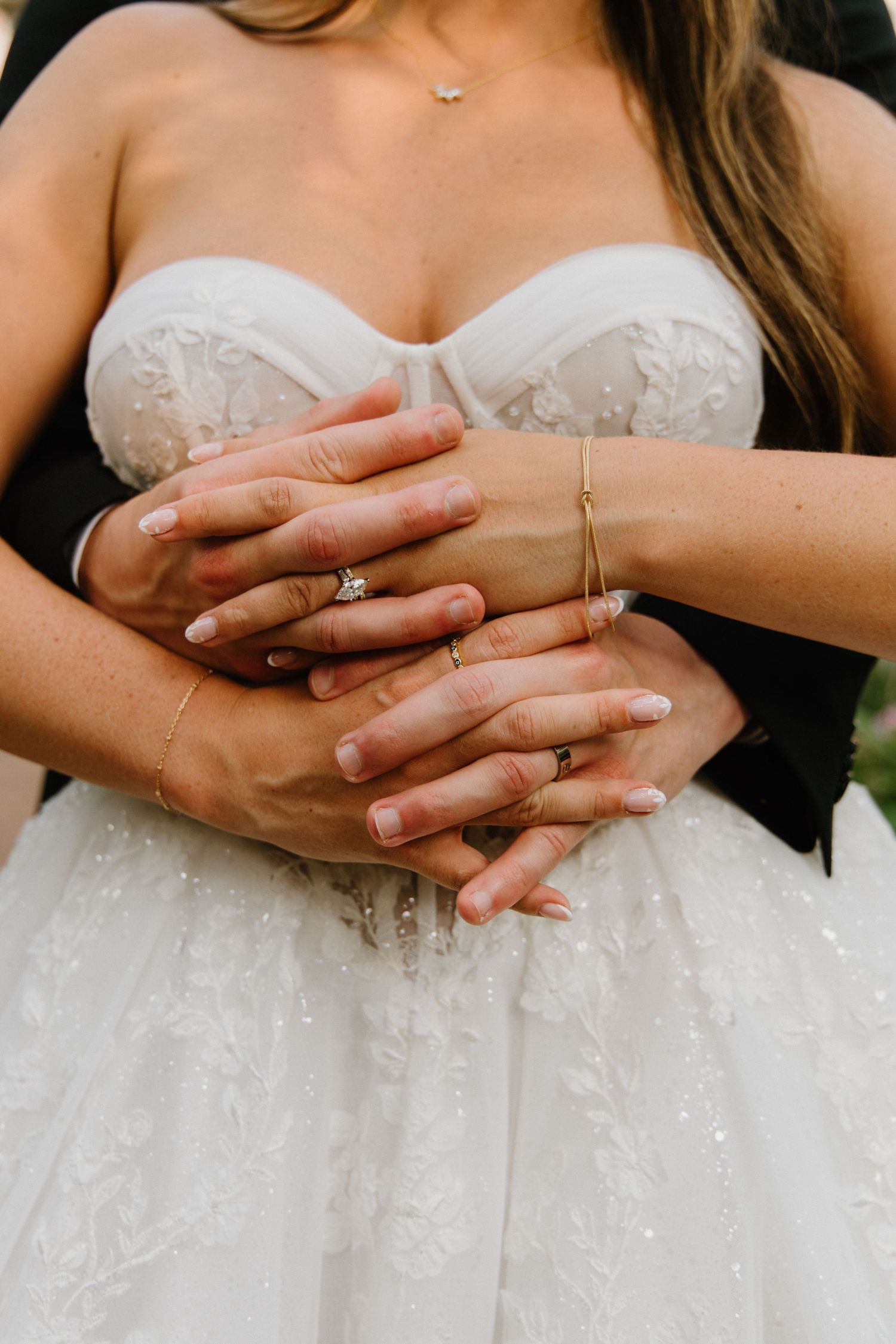 Close-up detail of hands showing wedding rings against a white beaded lace wedding dress.