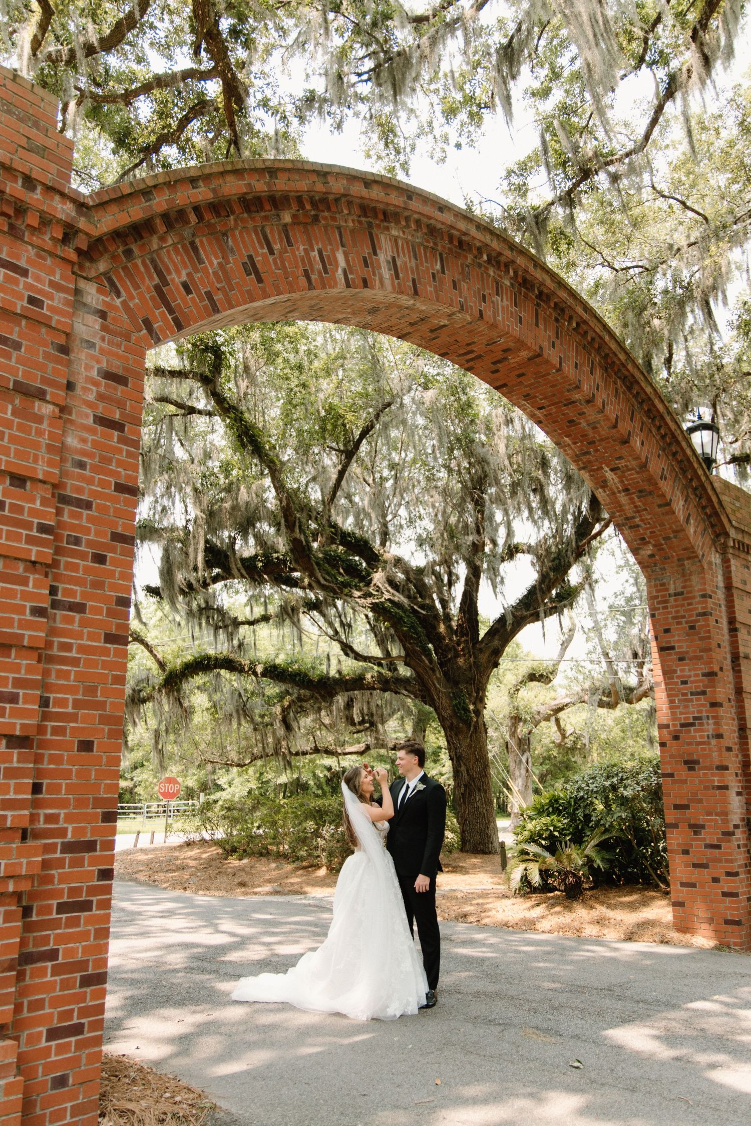 A romantic moment captured between figures beneath a majestic Spanish moss-draped oak archway at a rustic brick venue.