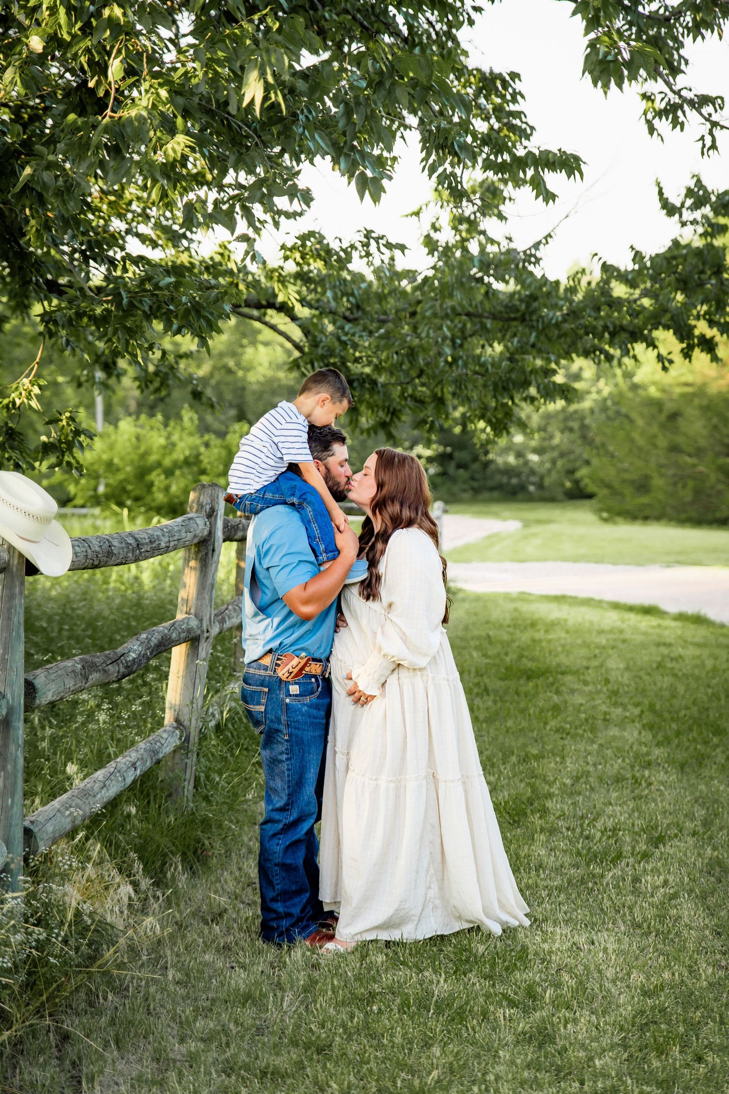 Romantic outdoor photoshoot by a wooden fence in a lush green field.