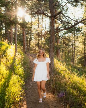A sunlit forest trail with golden light streaming through tall pine trees and lush green grass along the path at sunset.