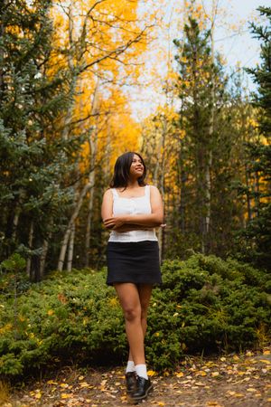 Fall forest scene showing a figure in a white tank top and black skirt standing on a path lined with golden aspen trees.