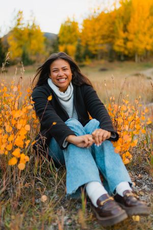 Someone sits in a field of golden wildflowers wearing light blue jeans and a white sweater during golden hour.
