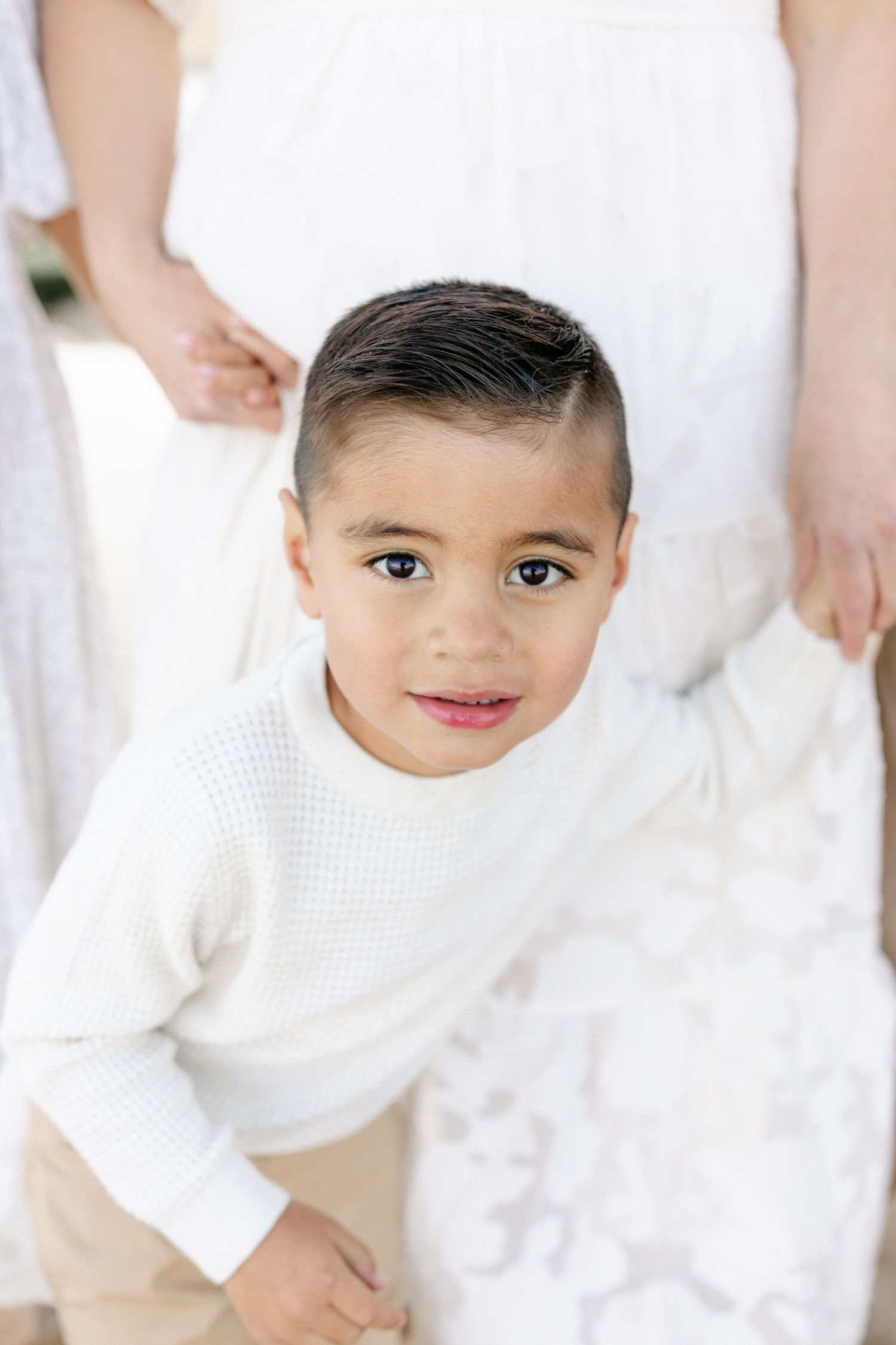 A child wearing a white knit sweater smiles gently while looking at the camera captured by Chelsee Rawe Photography.