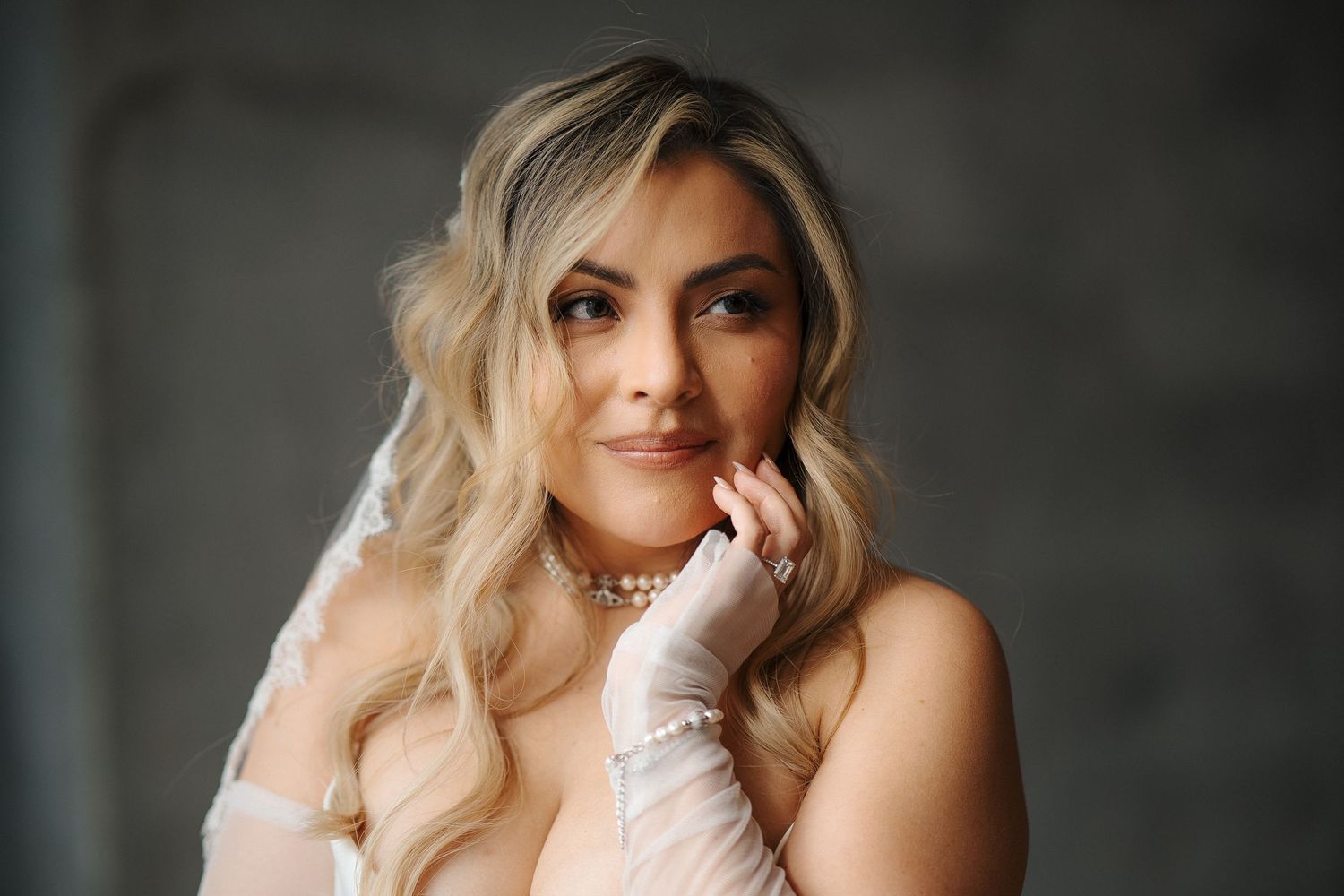 A portrait of someone with wavy blonde hair wearing white gloves against a dark background.