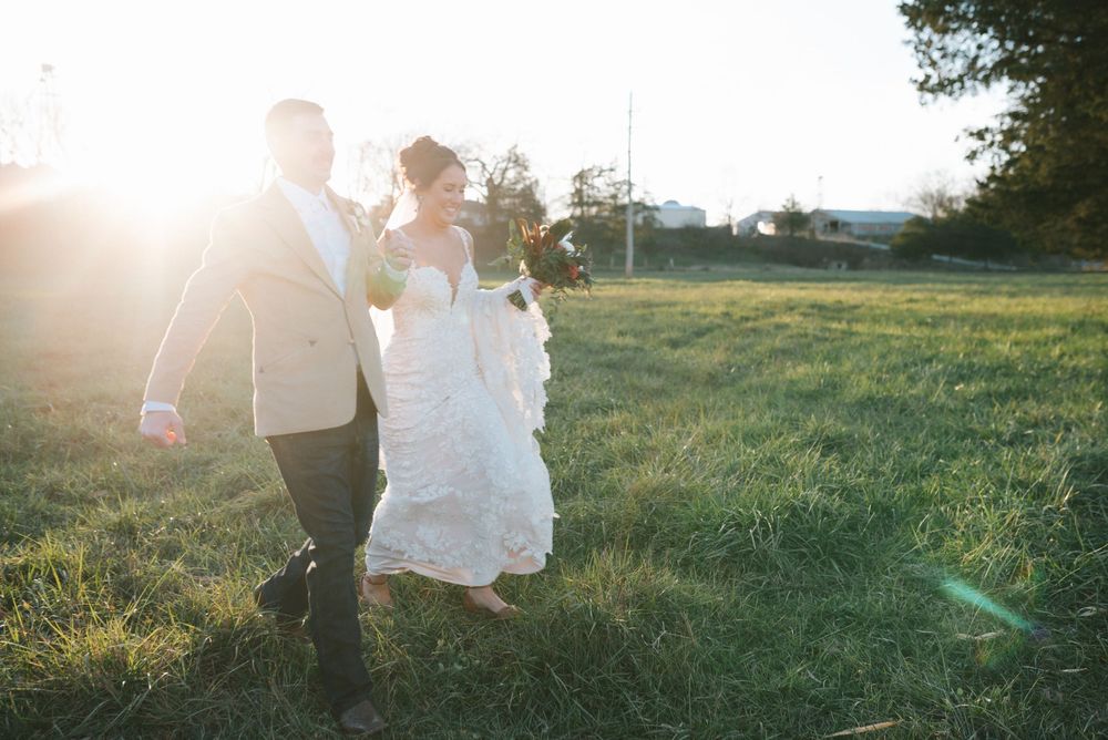 Couple walking through a grassy field at sunset after their wedding.