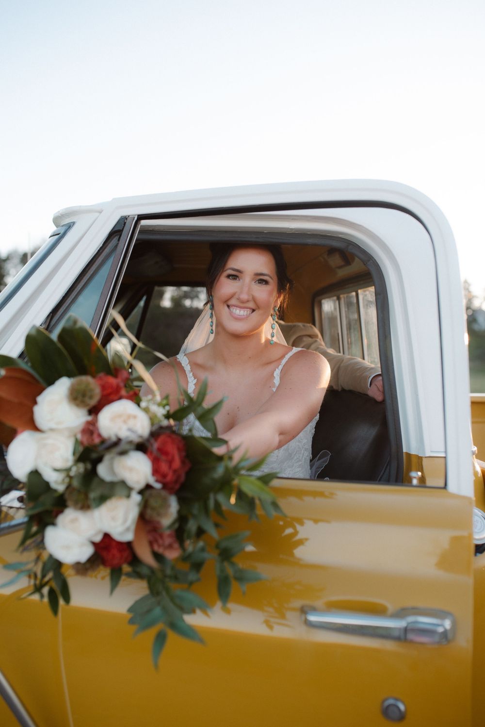 Yellow vintage truck with bridal bouquet of red and white flowers visible through driver's window.
