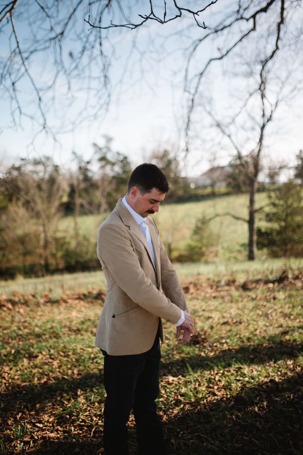 A person in formal attire adjusts their clothing during an outdoor photo session.