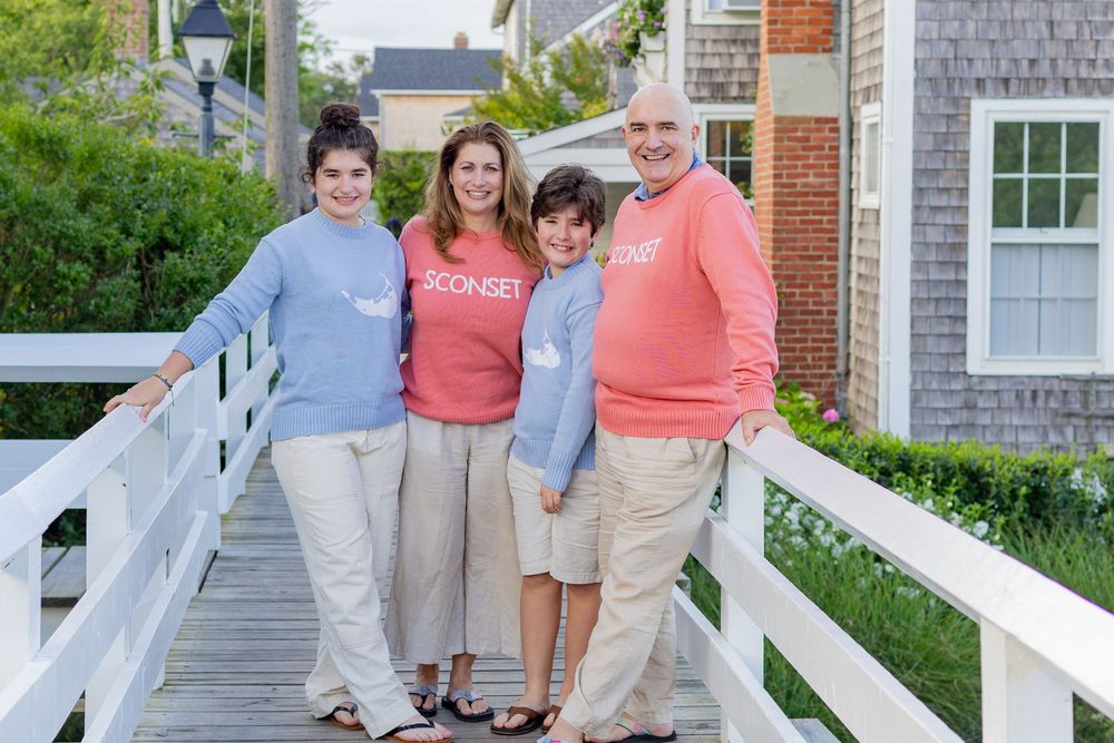 A family poses together in front of a classic New England house on a sunny day on the footbridge in Sconset village on Nantucket, MA