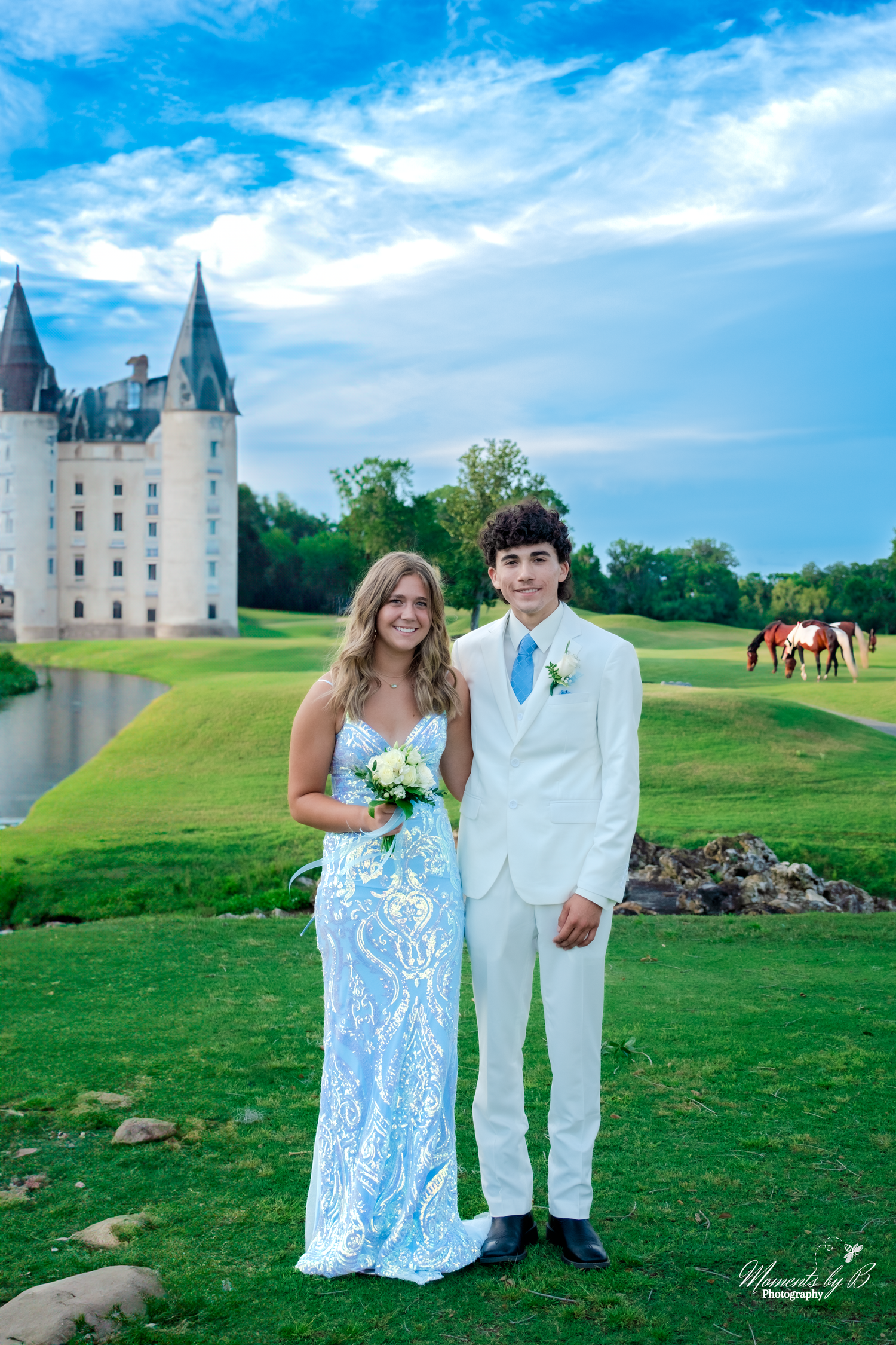 A formal couple poses on a lush green golf course under a bright blue sky with white clouds.