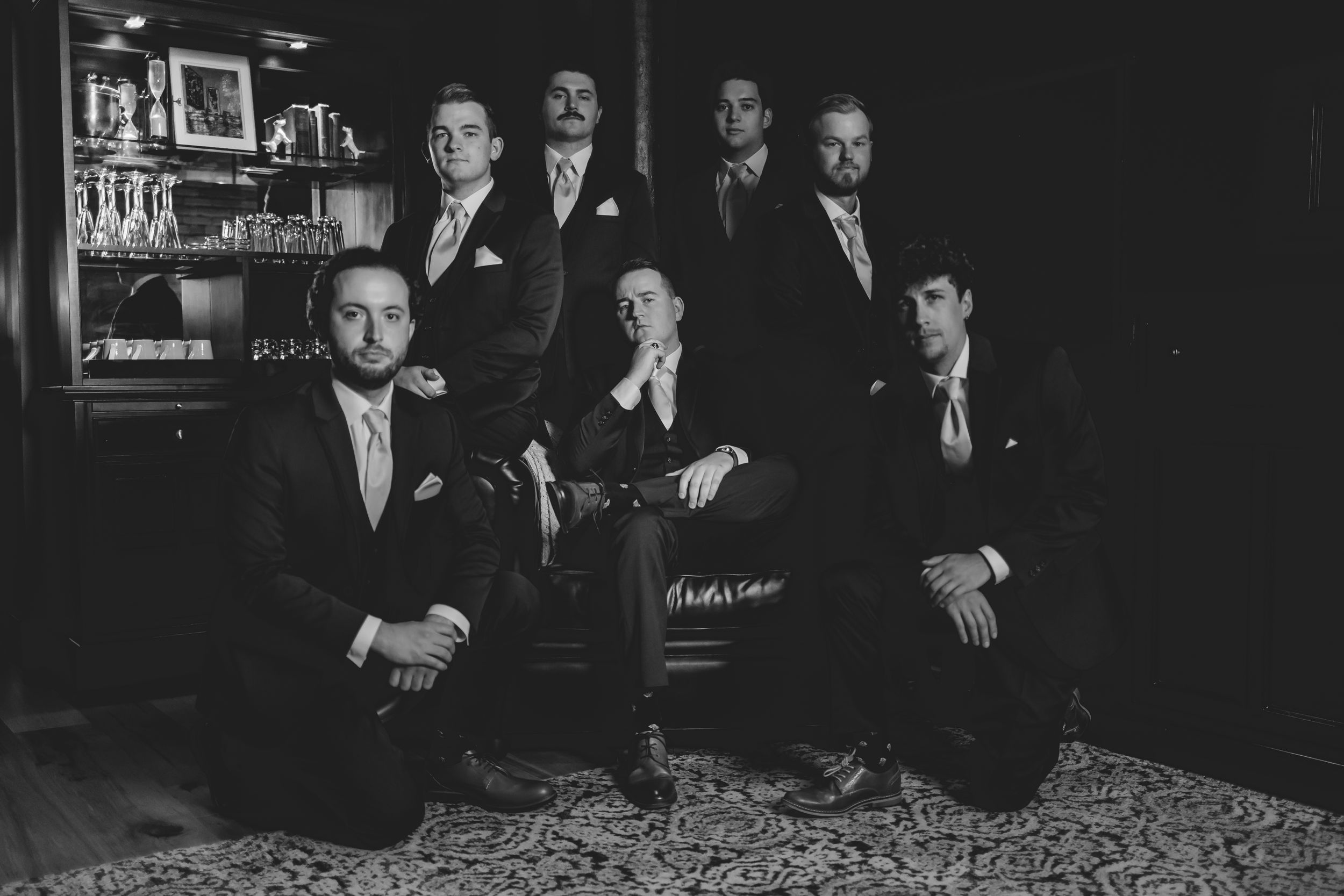 Black and white formal group photo showing a groom and groomsmen posed together in suits at a wedding venue.