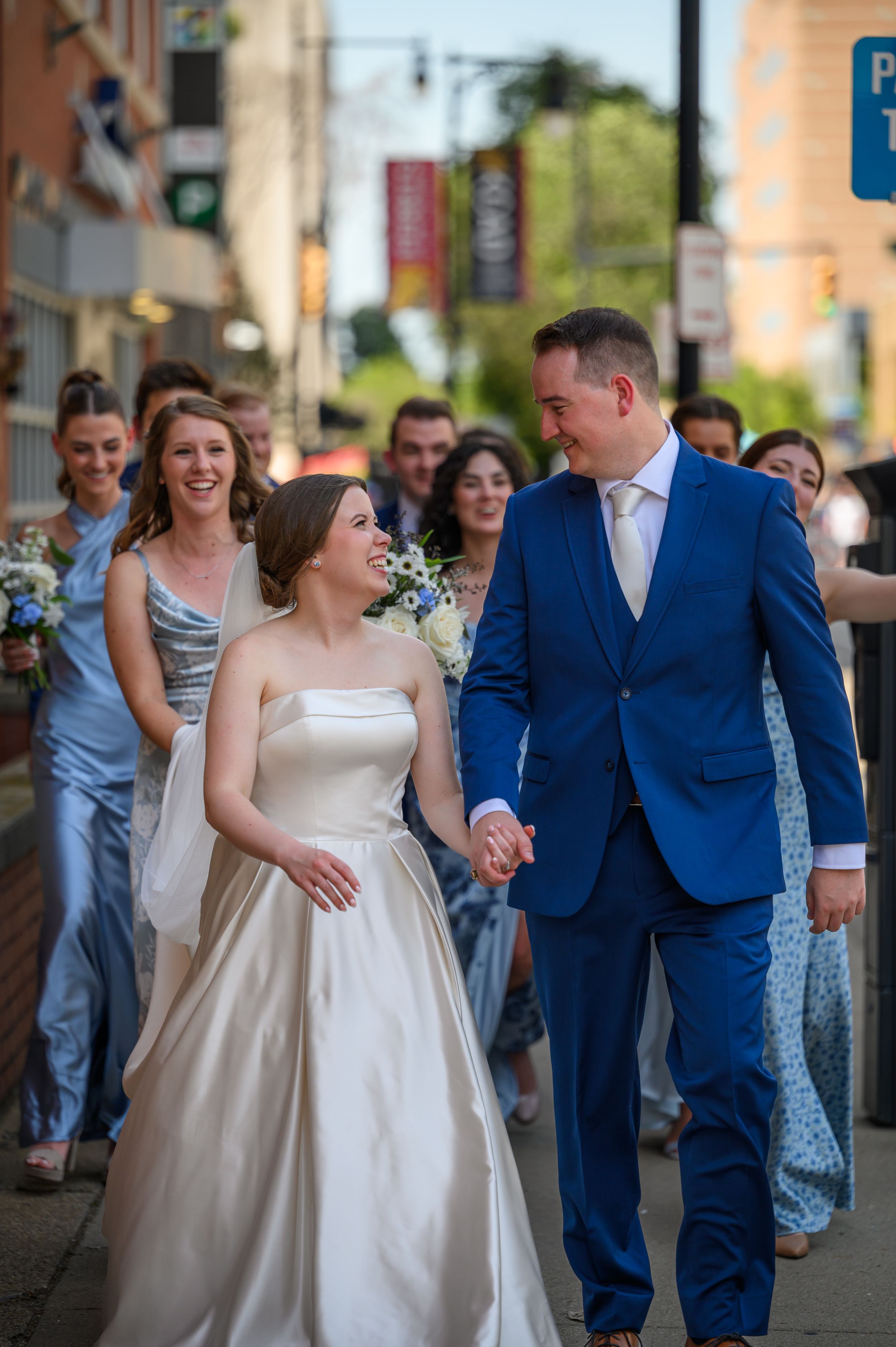 Wedding couple shares joyful moment walking together while guests follow behind on the streets of Downtown Grand Rapids Michigan