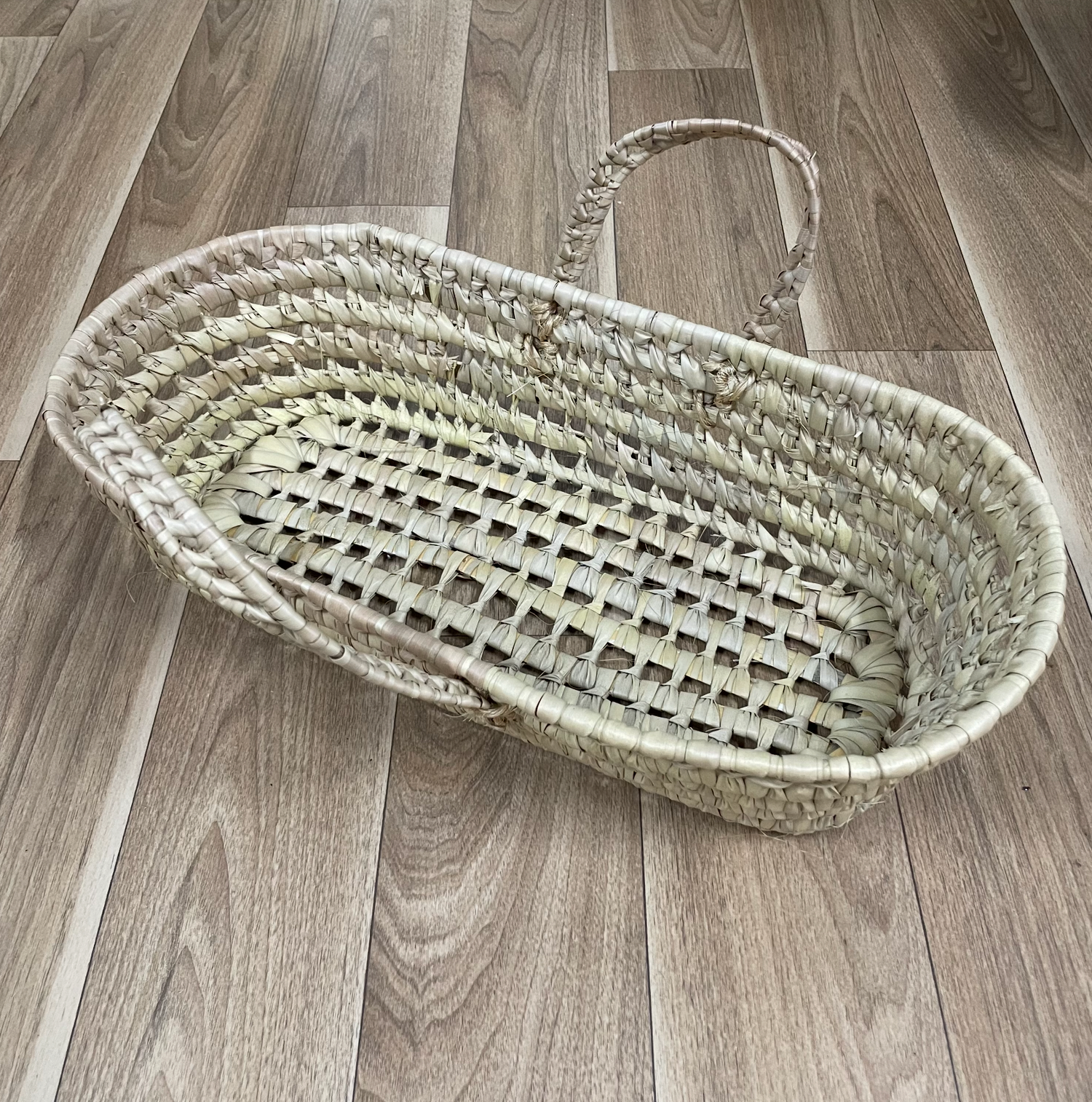 Oval woven basket displayed from different perspectives on hardwood flooring.