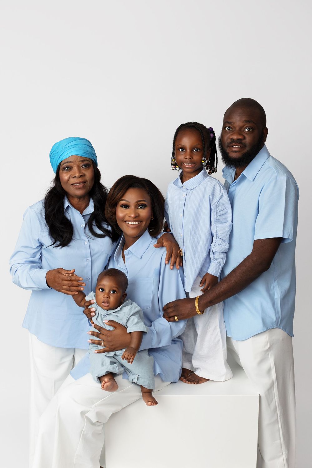 Multi-generational family wearing matching light blue shirts and white pants pose together for a studio portrait.