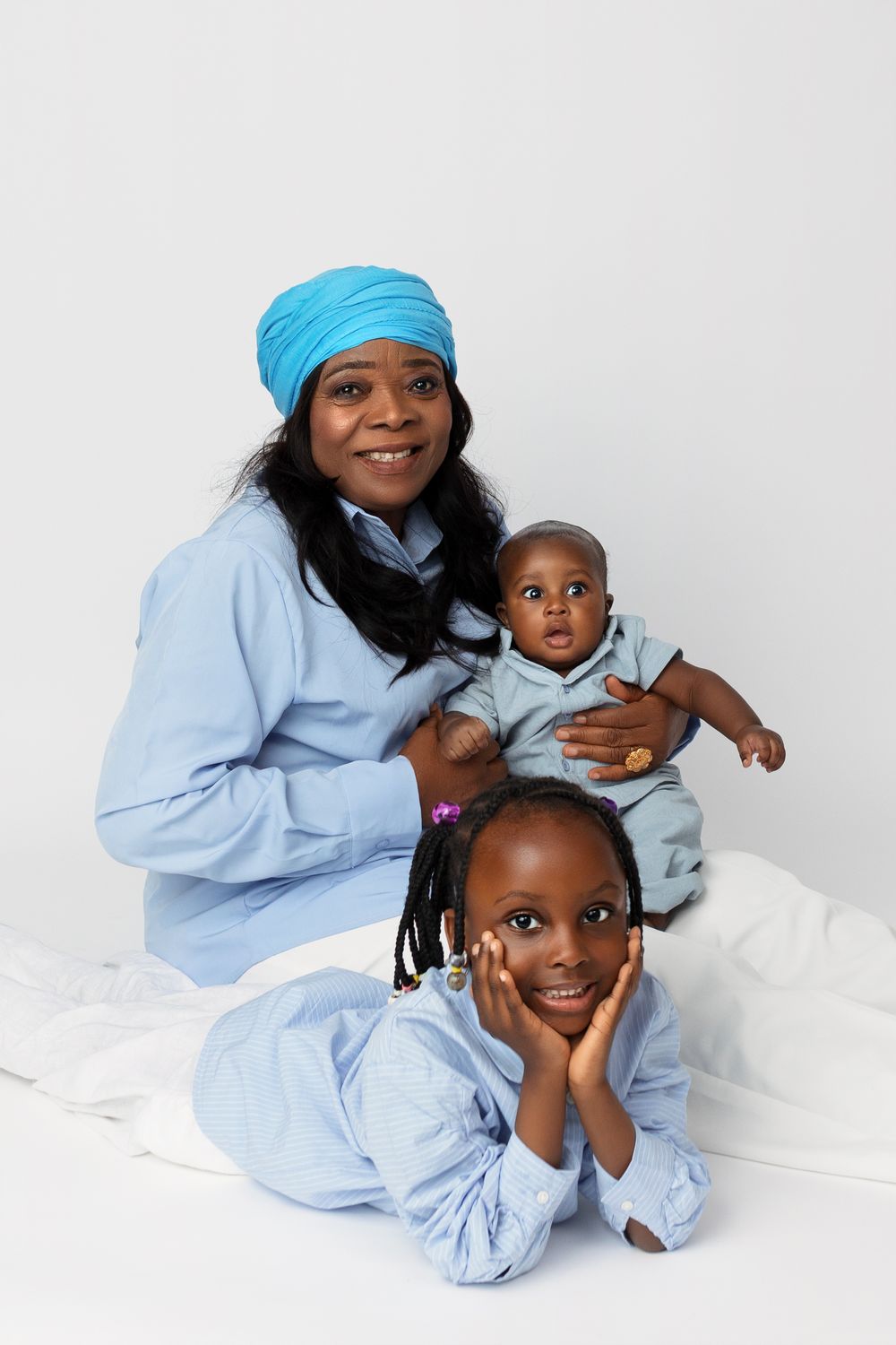Mother and children in matching light blue outfits pose together for heartwarming family portraits against white backdrop.