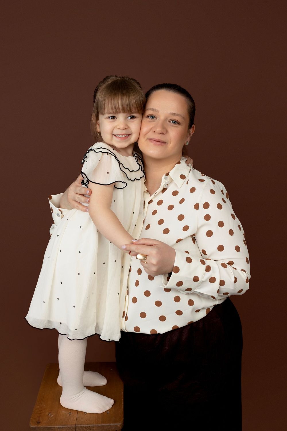 A series of four studio portraits showing a person in a polka dot top embracing a small child in a white dress.