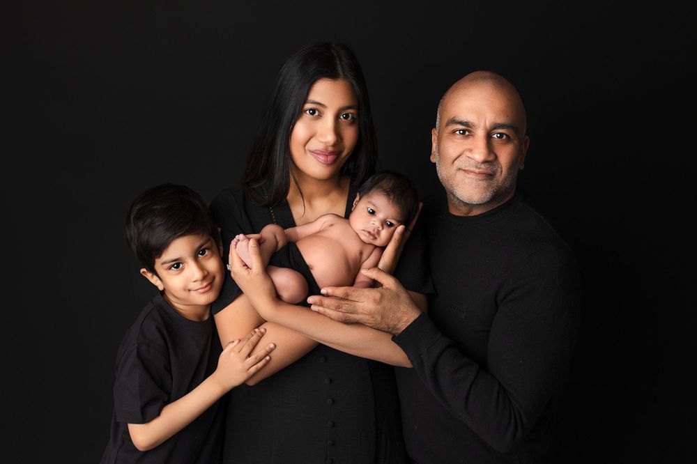 Professional studio portrait featuring a close-knit family of four against a dark background.