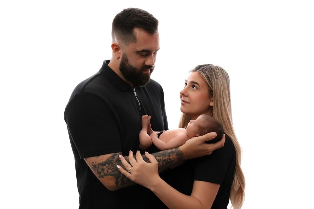 A couple wearing black outfits embraces in front of a white background during a studio photoshoot.