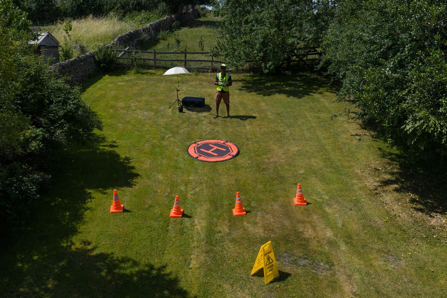 Remote-controlled drone practices takeoff and landing on a grassy field with orange cones and obstacles.