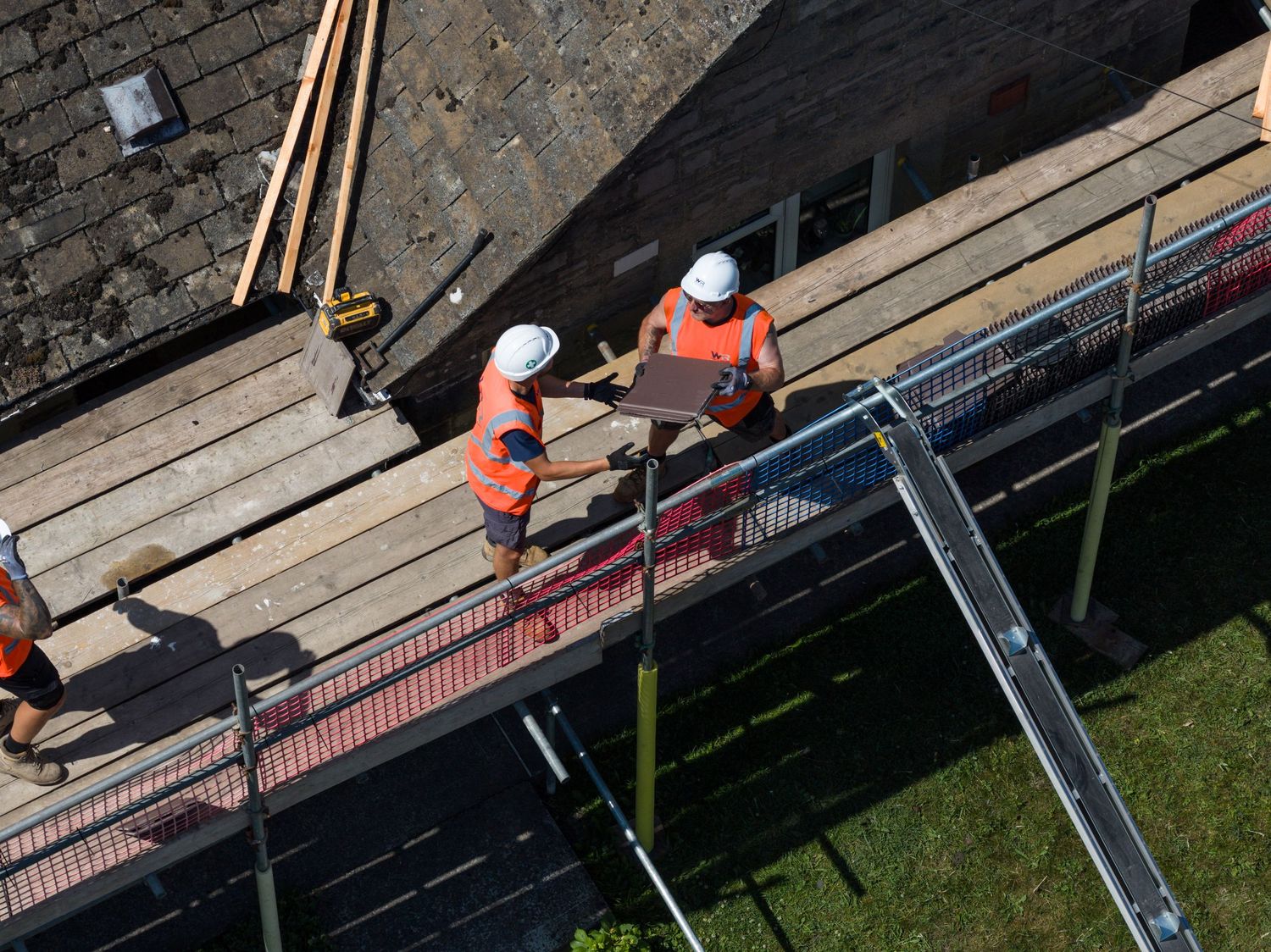 Construction workers installing wooden boards along a brick wall outdoors.