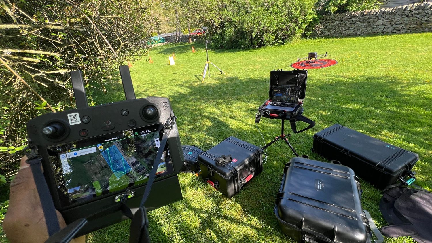 Drone flying equipment and remote control setup arranged on a table in a sunny backyard with green lawn.